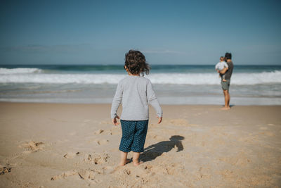 Rear view of girl with father standing on beach against sky