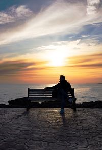 Man sitting on beach against sky during sunset