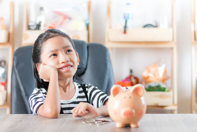 Girl sitting by piggy bank at table