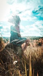 Woman sitting on field against sky