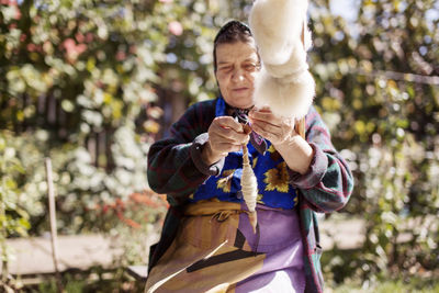 Senior woman winding thread on spindle while sitting at yard