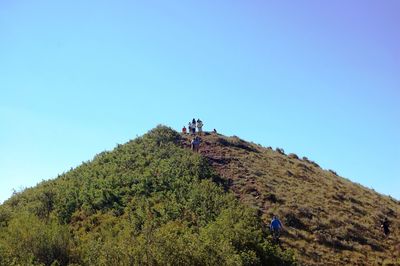 People walking on mountain against clear blue sky