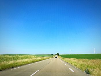 Road amidst field against clear blue sky