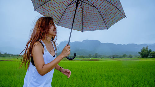 Smiling woman with umbrella standing on field