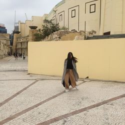 Full length of young woman holding purse standing on footpath against building