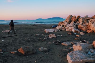 Scenic view of rocks at beach against sky during sunset