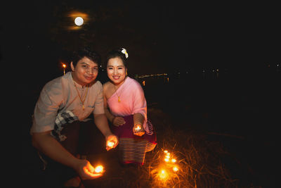 Portrait of couple holding lit tea lights at night