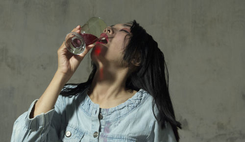 Young woman having drink while standing against wall