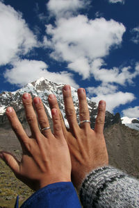 Cropped hands of couple showing rings against sky