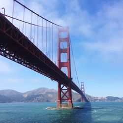 Low angle view of golden gate bridge over sea against blue sky during foggy weather