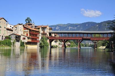 Bridge over river by buildings against blue sky