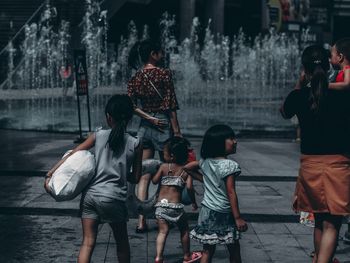 Rear view of people walking on footpath near fountain