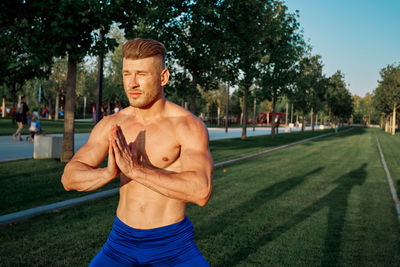 Portrait of shirtless man standing against trees