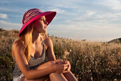 Young woman sitting on field against sky