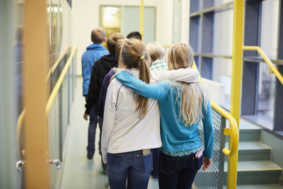 Rear view of girls walking arm around in school corridor