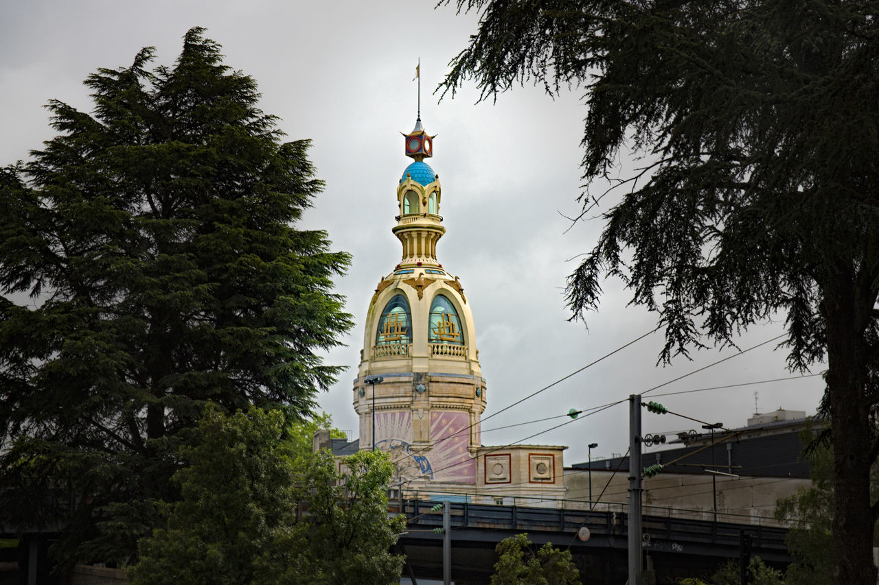 LOW ANGLE VIEW OF CLOCK TOWER AMIDST TREES AND BUILDINGS AGAINST SKY