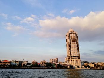 View of buildings by river against cloudy sky