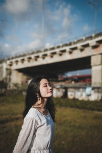 Young woman looking away while standing against sky