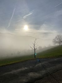 Street amidst field against sky during foggy weather