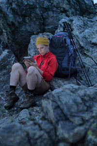 Full length of woman using digital tablet while sitting on rock formation