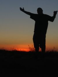 Silhouette man standing on field against sky during sunset