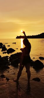 Full length of silhouette man standing on rock at beach against sky during sunset