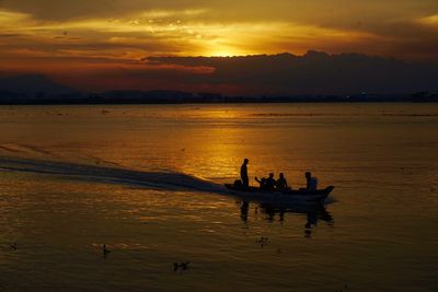 Silhouette people in sea against sky during sunset