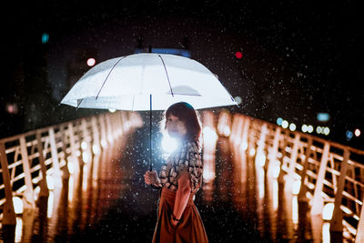 Woman holding umbrella standing at night during rainy season