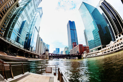 Modern buildings by river against sky in city