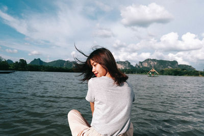 Woman sitting on wooden raft over lake against sky