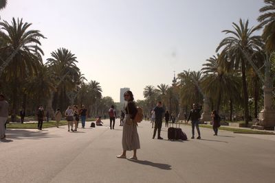 People walking on palm trees in city against clear sky