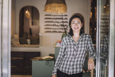 Portrait of smiling female sales clerk leaning on fashion boutique door handle