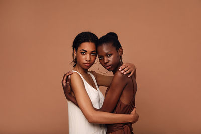 Portrait of lesbian couple embracing against brown background