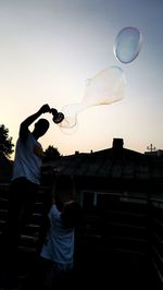 Low angle view of man holding bubbles against sky during sunset