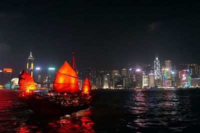 Illuminated city by calm sea at night