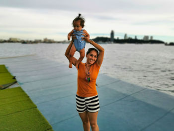 Full length of mother and daughter standing at shore against sky