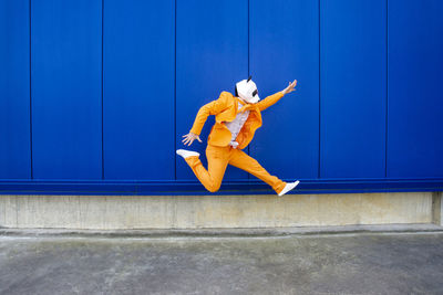 Low angle view of person jumping against blue wall