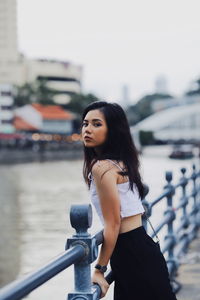 Side view of young woman standing at railing by river in city