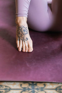 Crop anonymous barefoot of female ith tattoo on foot in leggings lying on yoga mat on the floor at home