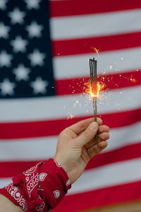 Cropped hand of person holding illuminated sparklers against american flag