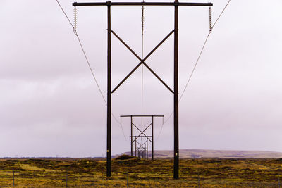 Low angle view of electricity pylon on field against sky
