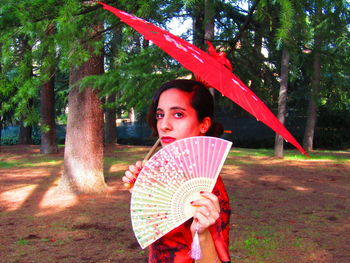 Portrait of woman holding red while standing on tree