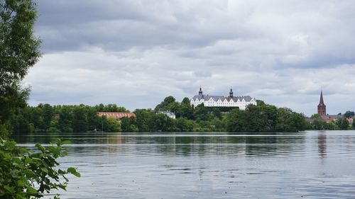 View of building by lake against cloudy sky