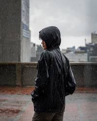 Young man wearing raincoat while standing outdoors during rainy season