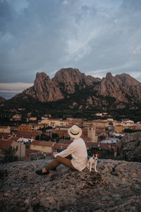 Side view of woman sitting on rock against sky