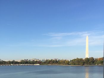 Washington monument by lake against blue sky