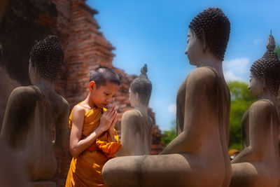 Boy praying while standing by buddha statue