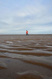 Boy walking on beach against sky