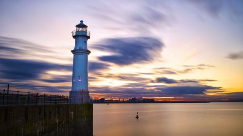 Lighthouse by sea against sky during sunset