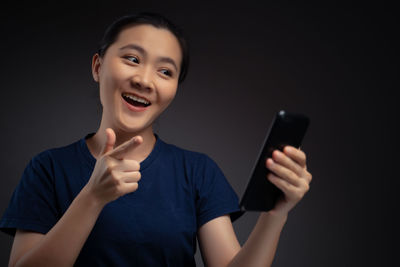 Portrait of smiling young woman using smart phone against black background